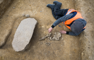 A man laying beside buried bones and a stone slab.